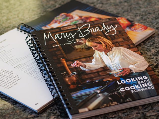 photo of a cookbook opened on a marble table with the cover of the cookbook laying on top of it.